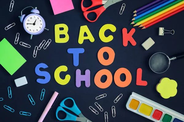 La escuela y los artículos de papelería están dispersos en el fondo negro. En el centro de la inscripción en letras de colores, Back to School . — Foto de Stock
