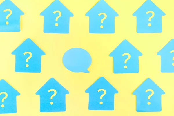 Etiquetas azuis na forma de uma casa em um fundo amarelo, eles são escritos com pontos de interrogação. No centro há um adesivo de bolha vazio. Foto do topo . — Fotografia de Stock