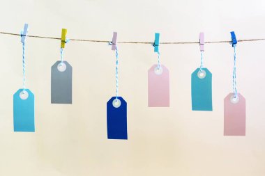 Bir fotoğrafı soluk bej arka plan etiketleri. Çok renkli boş etiketleri clothespins ile tutturulmuş ip dayan. Parlak düzen, alay etmek yukarıya.