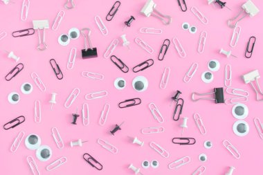 Klipler ve kukla gözler pembe bir arka plan üzerinde ciddi bir yüz. Büro aksesuarları düzensizce dağılmış. Alışılmadık bir arka plan klipleri ve büro düğmeleri. Güzel resim üst.