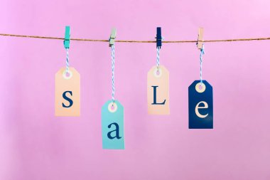 Etiketleri clothespins ile bağlı bir ip dayan. Yazıt satışı var. Pembe bir arka plan üzerinde parlak fotoğraf.