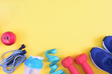 Sarı yüzeyde kırmızı dambıl, spor ayakkabı, bir şişe ve bir elma vardır. Bir yazıt, yukarı alay etmek için en iyi yer. Parlak fitness arka plan.