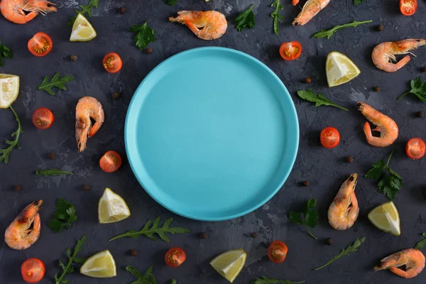Boş bir mavi çanak koyu dokulu arka plan ortasında yatıyor. Çevresinde limon, rucola, biber ve karides dağılmış. Üstten, güzel fotoğraflar alay.
