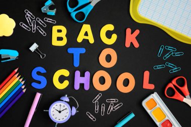 Siyah bir arka plan üzerine düzensizce Kırtasiye yayılır. Renkli harfler yazıt ortasında okula geri. Üstten güzel parlak fotoğraf.