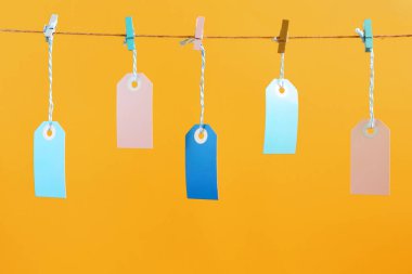 Bir fotoğrafı parlak turuncu arka plan etiketleri. Beş çok renkli boş etiketleri clothespins ile sabitlenmiş bir ip dayan. Parlak düzen, alay etmek yukarıya.