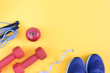 Bir modeli ile spor Tema metni için bir yer. Fitness arka plan. Halter, spor ayakkabı, atlama ipi, kırmızı elma parlak sarı bir arka plan üzerinde yer alır. Güzel resim üst.