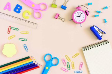 Açık bej arka planı üzerinde ataç, bir dizüstü bilgisayar, bir çalar saat ve okul malzemeleri vardır. Yazmak için boş bir alana ortasına kadar alay et. Parlak fotoğraf.