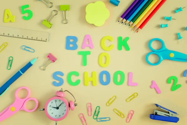 In the center of table the inscription is BACK TO SCHOOL, made in colored letters. Bright colored school and office supplies are arranged around. Bright layout.