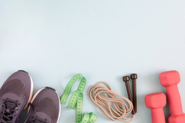 Metin için yer ile fotoğraf. Spor ayakkabı, halter ve soluk mavi arka plan üzerinde bir ip atlama.