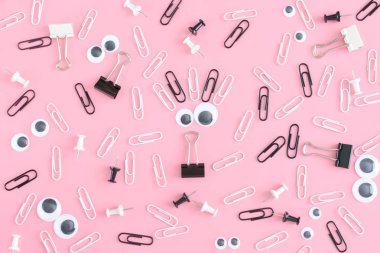 An unusual pink background with a pattern of stationery chaotically scattered. Smiley from puppet eyes and clips in the center. Photo from the top. clipart