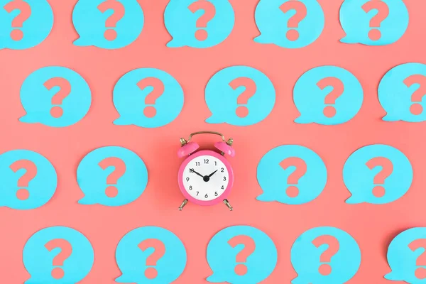 Many pink stickers with question marks are on the pink background. In the center is a small pink alarm clock. Concept, a matter of time.