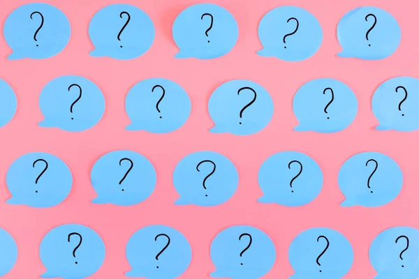 Question marks are written on blue stickers in the form of a bubble. Blue paper pasted on a pink background. Bright unusual background.