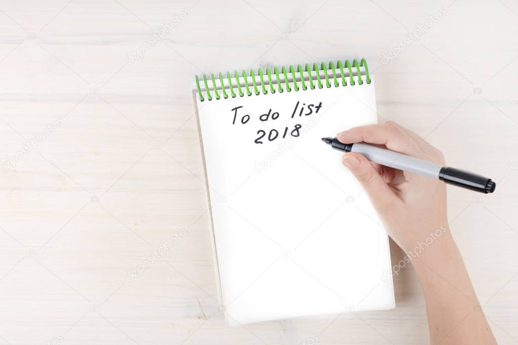 A to-do list in a notepad on spirals. Place for text. A girl's hand holds a marker. Mock ap.
