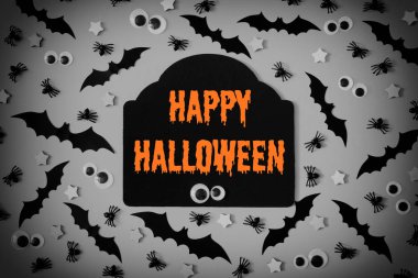 Dekoratif yarasalar, yıldız ve kukla gözleri çok gri bir arka plan ile kaplı. Ortasında figürlü bir tablet ile bir yazıt vardır. Mutlu Helloween parlak turuncu harflerle yazılmış.