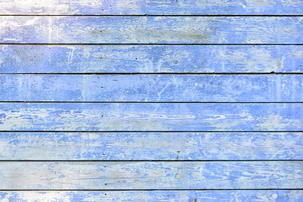 The wall is made of flat horizontally painted boards painted with blue paint. Old faded coating cracked and scuffed. Beautiful light background.