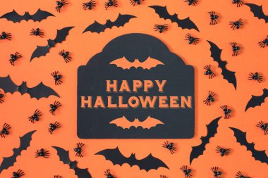 Dekoratif örümcekler ve Cadılar Bayramı yarasalar bir turuncu zemin üzerine yerleştirilir. Ortasında yazıt mutlu Halloween ile figürlü bir tablet var. Üst parlak fotoğraf.