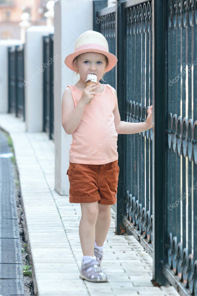 A little girl with blond hair goes and eats ice cream. Beautiful portrait in full growth.