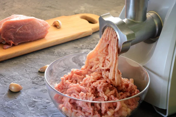 The electric meat grinder makes minced meat. The process of cooking close-up. In the background, the meat with spices in the blur. Useful home food.