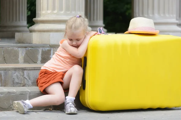 小女孩睡着了 把胳膊肘靠在一个大黄色的手提箱上 一个漂亮女孩的肖像 背景模糊 — 图库照片
