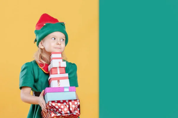 小女孩在圣诞节精灵服装与礼品绿色和黄色背景 — 图库照片