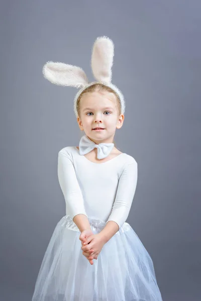 Little girl in white Easter bunny costume on gray background
