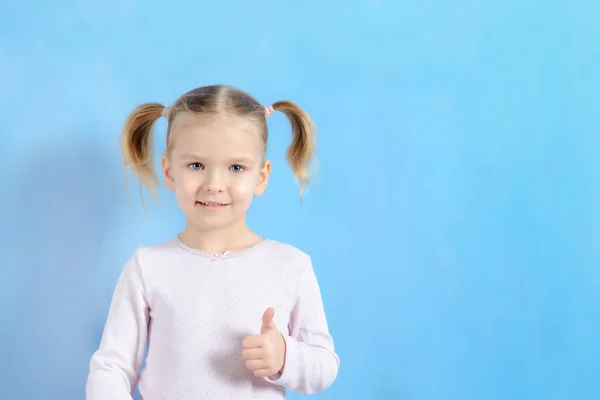 Ein kleines Mädchen mit einem Haar und zwei Schwänzen. niedliches Baby mit blonden Haaren zeigt Zeichen super. — Stockfoto