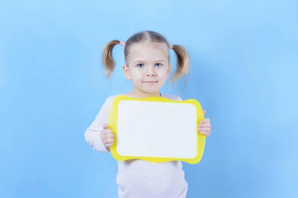 Ein kleines Mädchen mit einem Haar und zwei Schwänzen. ein niedliches Kind mit blonden Haaren hält ein Schild mit Platz für Text. — Stockfoto