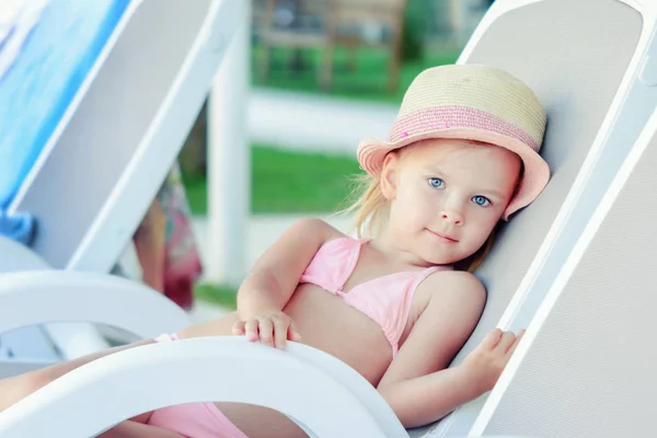 Una niña en un sombrero está tomando el sol en una tumbona. Hermoso bebé de vacaciones . — Foto de Stock