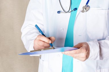 Medic not defterinde kalemle bir şeyler yazıyor. Beyaz tıbbi elbiseli bir adam..