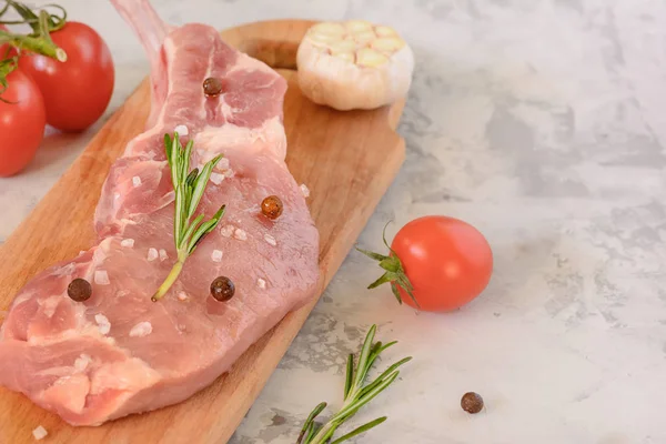 Кусок свежего мяса свинины лежит на разделочной доске, наряду с чесноком и помидорами. Подготовка к приготовлению стейка . — стоковое фото