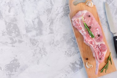 Bir parça çiğ et, bir kesme tahtasında yatıyor. Biber ve biberiye sahip domuz bifteği. Gri taştan arka planda boşluk Kopyala.