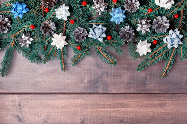 Kompozycja Świąteczna z przestrzenią kopiowania. Gałęzie choinki są pięknie ułożone na drewnianym tle. Świerkowe gałęzie ozdobione kokardami, szyszki srebrne i małe czerwone jagody. — Zdjęcie stockowe