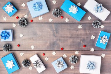 Yay, kırmızı çilek, gümüş konileri ve kar taneleri ile küçük mavi ve beyaz kutular, bir daire halinde düzenlenmiştir. Ahşap arka plan üzerinde kopya alanı ile Noel kompozisyon. Şenlikli düzen.