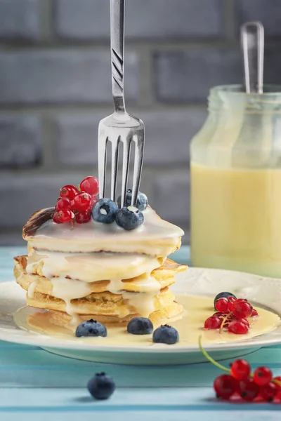 Delicious pancakes with condensed milk and berries. Dessert with blueberries and red currants. A fork is inserted into a stack of freshly fried pancakes — Stock Photo, Image