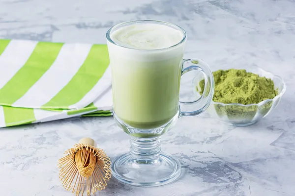Matcha green tea latte with matcha powder and bamboo whisk. Healthy drink in a transparent glass close-up