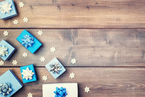 White and blue gift boxes are laid out in a corner of the wooden background. Among them are white snowflakes. — Stock Photo, Image