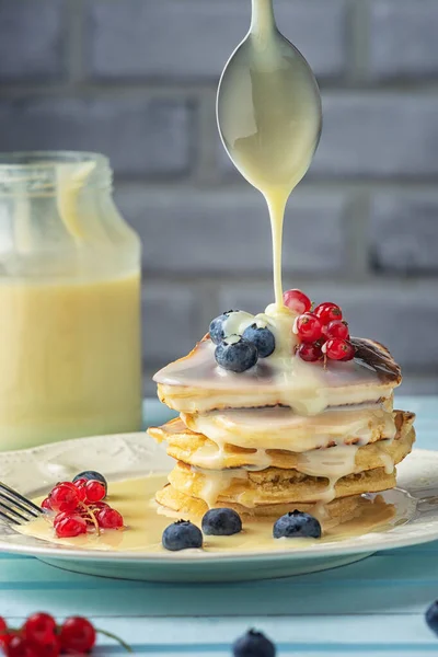 A stack of freshly prepared pancakes is poured with condensed milk. Tasty breakfast with fresh berries — Stock Photo, Image