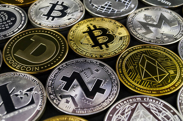 Много криптовалютных монет лежат на темной поверхности
