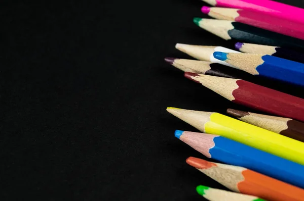 Många färgglada blyertspennor ligger på en svart bakgrunds papper — Stockfoto
