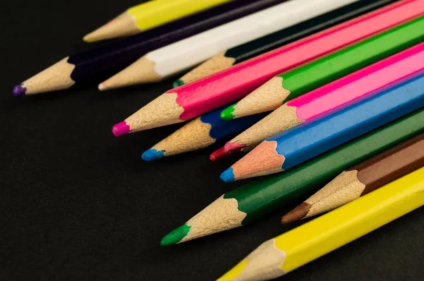 Många färgglada blyertspennor ligger på en svart bakgrunds papper — Stockfoto