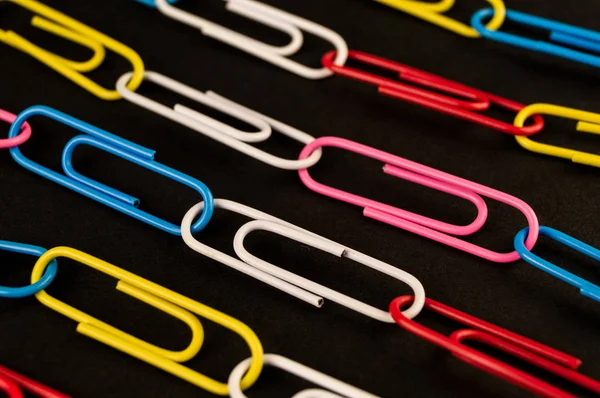 De nombreux trombones colorés reposent sur un papier de fond noir — Photo
