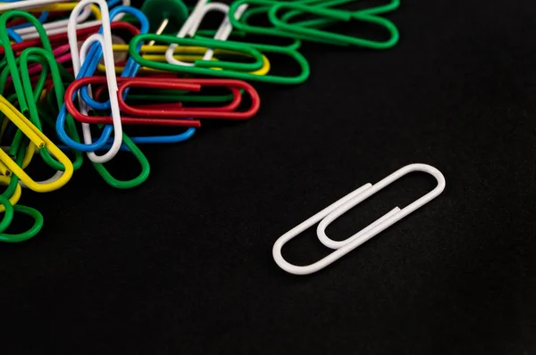 Many colorful paper clips lie on a black background paper — Stock Photo, Image