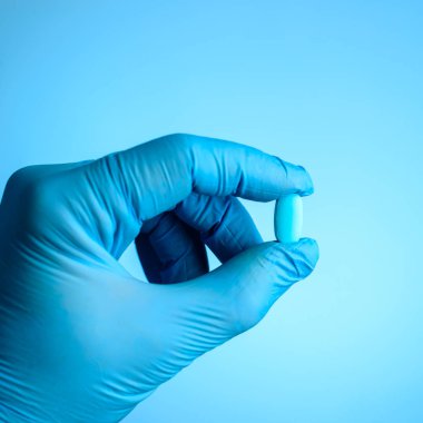 Unidentified doctor hand with latex glove holding a pill or caps clipart