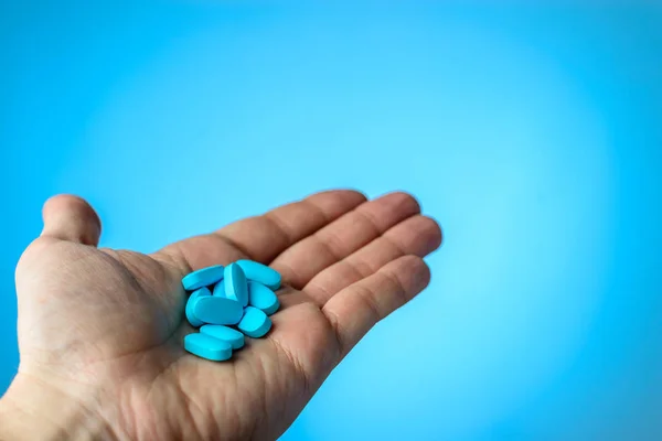 Las pastillas azules en el paciente por las manos sobre el fondo azul. El cuidado de la — Foto de Stock