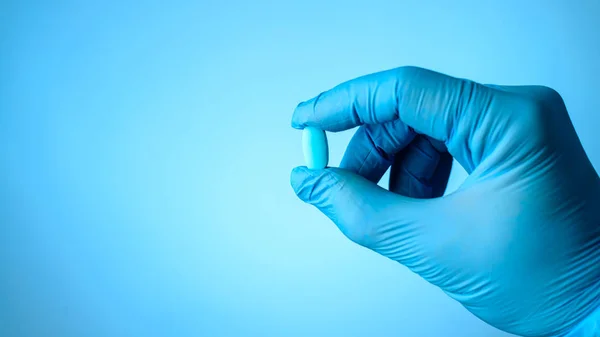 Unidentified doctor hand with latex glove holding a pill or caps