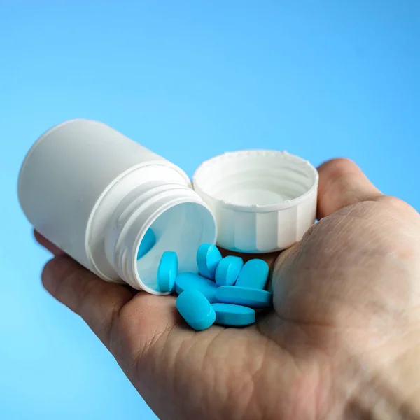 Las pastillas azules en el paciente por las manos sobre el fondo azul el primer plano. Carin. — Foto de Stock