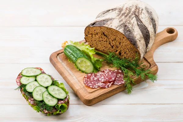 Pão e um sanduíche com salame e pepino fresco — Fotografia de Stock