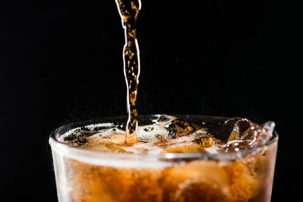 Stream of cola is poured into a glass with ice — Stock Photo, Image