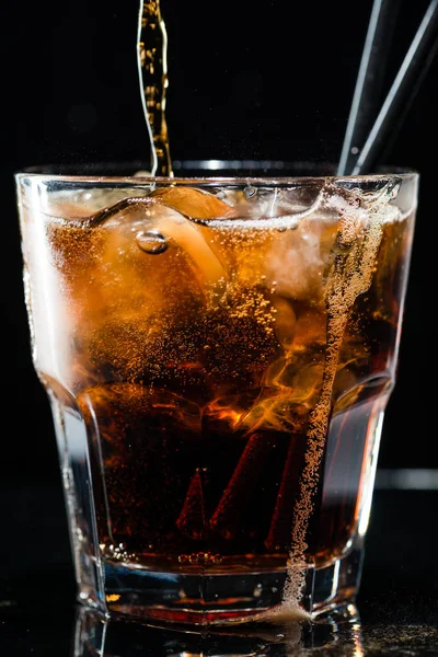 Stream of cola is poured into a glass with ice — Stock Photo, Image