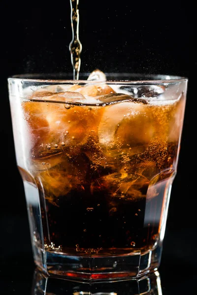 Stream of cola is poured into a glass with ice — Stock Photo, Image